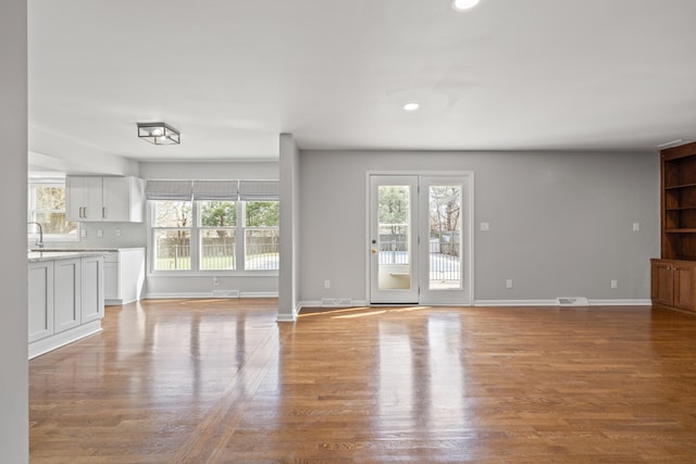 unfurnished living room with visible vents, a sink, baseboards, and wood finished floors