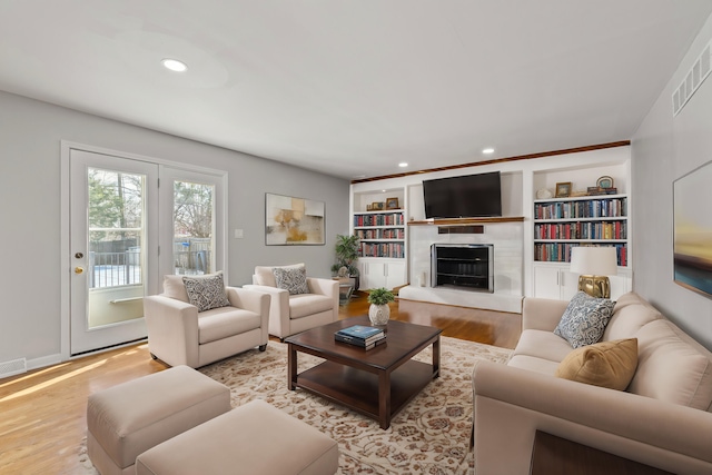 living area featuring built in shelves, wood finished floors, visible vents, recessed lighting, and a fireplace with raised hearth