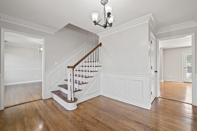 stairs featuring a decorative wall, baseboards, ornamental molding, wood finished floors, and a notable chandelier