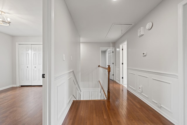 corridor featuring an upstairs landing, a decorative wall, attic access, and wood finished floors