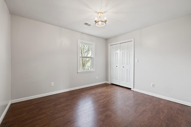 unfurnished bedroom featuring visible vents, baseboards, a closet, a notable chandelier, and dark wood-style flooring