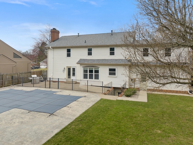 rear view of house featuring a patio, fence, a shingled roof, a chimney, and a lawn