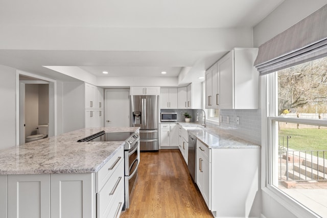 kitchen featuring wood finished floors, a kitchen island, a sink, appliances with stainless steel finishes, and backsplash