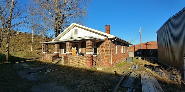 view of home's exterior with covered porch, a chimney, central AC, and brick siding