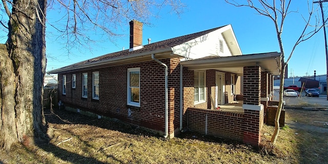 view of side of home featuring a porch, brick siding, and a chimney