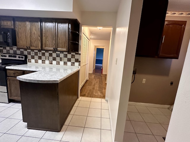 kitchen with black microwave, light tile patterned floors, a peninsula, light countertops, and stainless steel electric range