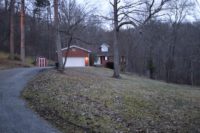 view of front of home featuring a forest view, aphalt driveway, an outbuilding, an attached garage, and a storage unit