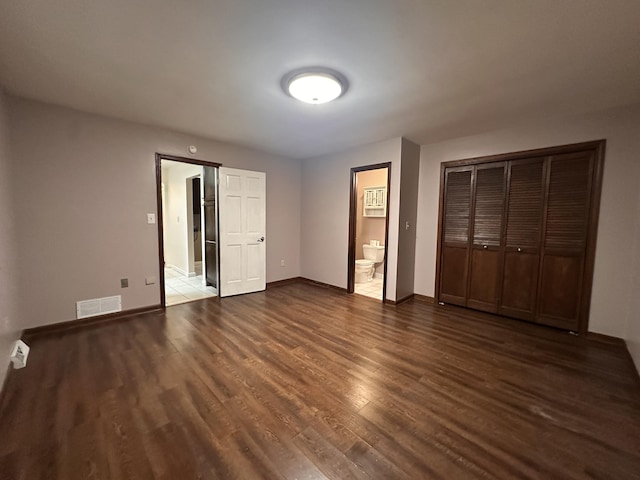 unfurnished bedroom with dark wood-type flooring, visible vents, baseboards, a closet, and ensuite bath