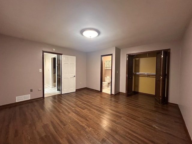 unfurnished bedroom featuring ensuite bathroom, wood finished floors, visible vents, baseboards, and a closet