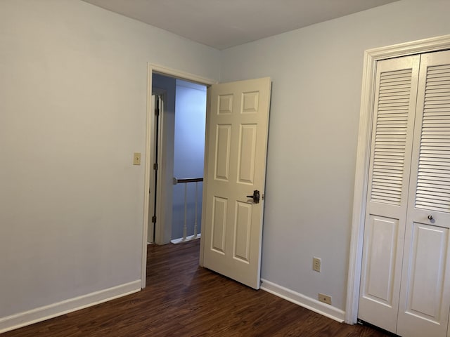 unfurnished bedroom with a closet, dark wood finished floors, and baseboards