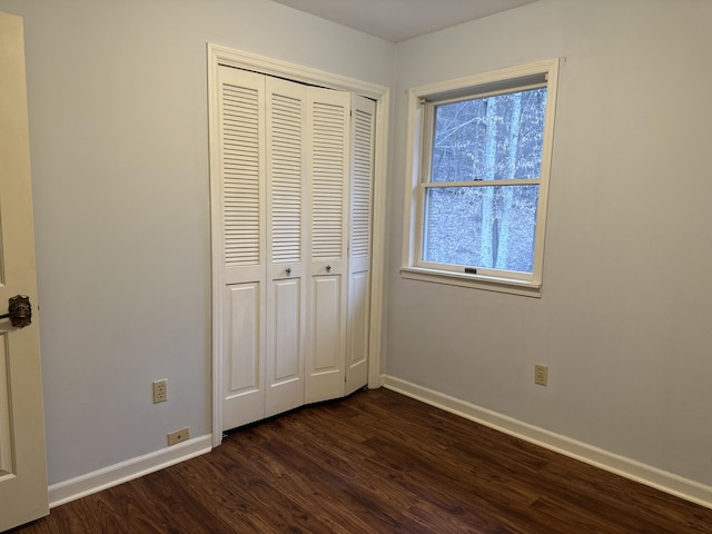 unfurnished bedroom with dark wood-style floors, baseboards, and a closet