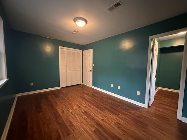 unfurnished bedroom with baseboards, visible vents, dark wood finished floors, and a closet