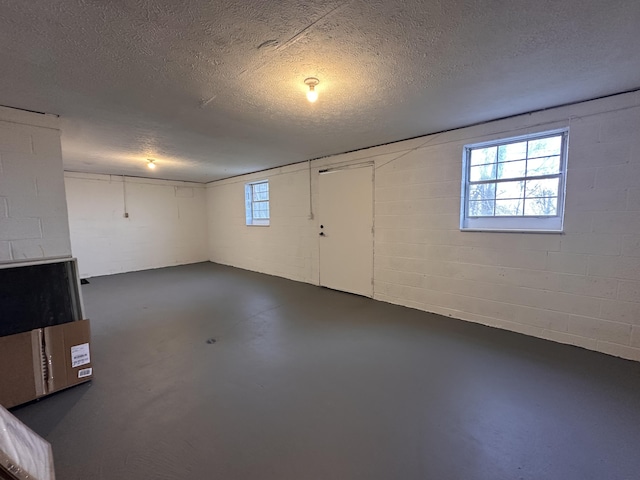 basement with concrete block wall, a textured ceiling, and a wealth of natural light