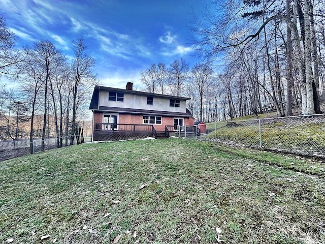 rear view of house with a wooden deck, a chimney, fence, a yard, and brick siding