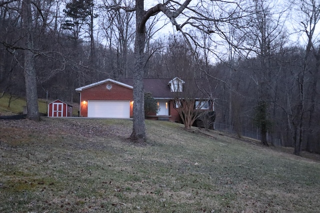 view of front of property with an attached garage, a storage shed, brick siding, a forest view, and a front yard