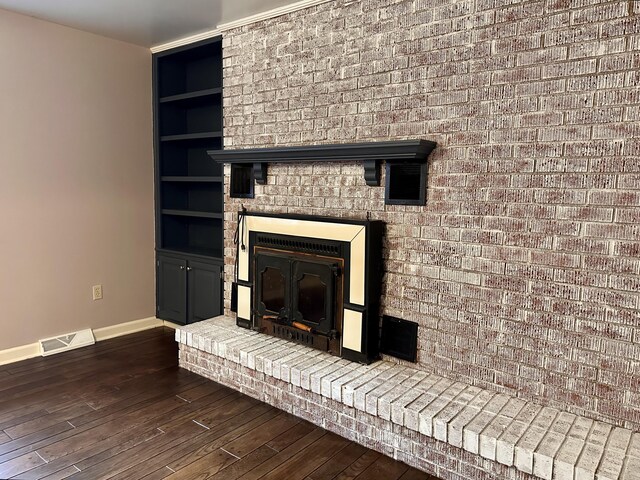 unfurnished living room with built in features, dark wood-type flooring, a ceiling fan, a brick fireplace, and baseboards