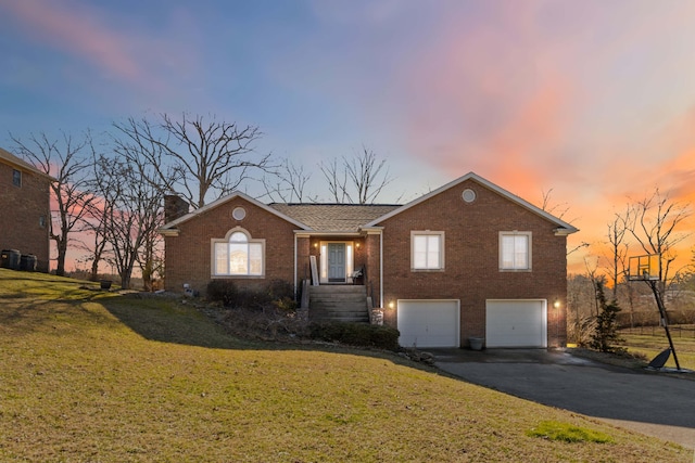 view of front facade featuring aphalt driveway, brick siding, a chimney, an attached garage, and a front yard