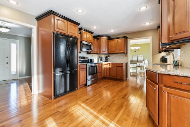 kitchen with light stone counters, appliances with stainless steel finishes, light wood-style floors, brown cabinetry, and a sink