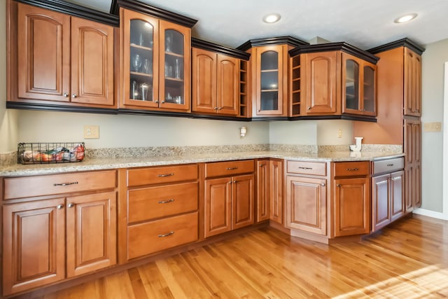 kitchen with light wood finished floors, brown cabinetry, light stone counters, and recessed lighting