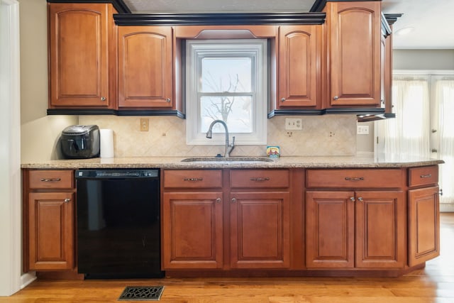 kitchen featuring black dishwasher, visible vents, a sink, light stone countertops, and light wood-type flooring