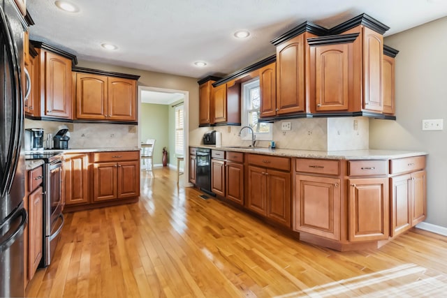 kitchen featuring light stone counters, brown cabinetry, a sink, light wood-type flooring, and black appliances