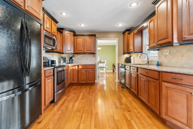 kitchen featuring light wood finished floors, appliances with stainless steel finishes, brown cabinetry, and a sink