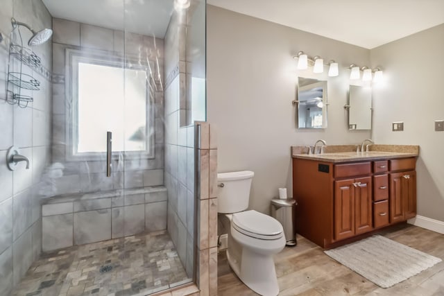 full bathroom with toilet, a stall shower, vanity, wood finished floors, and baseboards