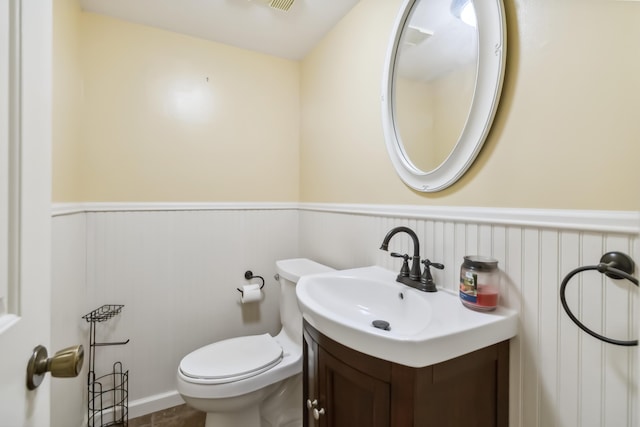 bathroom featuring toilet, a wainscoted wall, and vanity