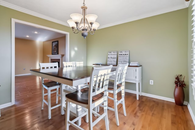 dining space with crown molding, a fireplace, a chandelier, and wood finished floors