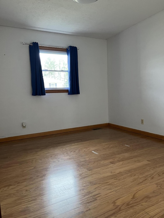 empty room with visible vents, a textured ceiling, baseboards, and wood finished floors