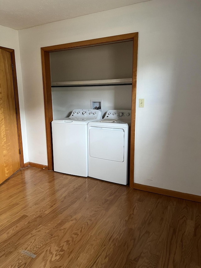 laundry area with laundry area, wood finished floors, washing machine and dryer, and baseboards