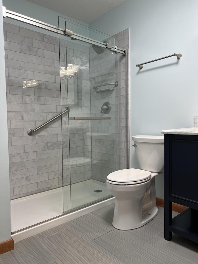 bathroom with toilet, a stall shower, vanity, and baseboards