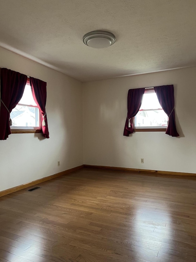 unfurnished room featuring baseboards, a textured ceiling, visible vents, and wood finished floors