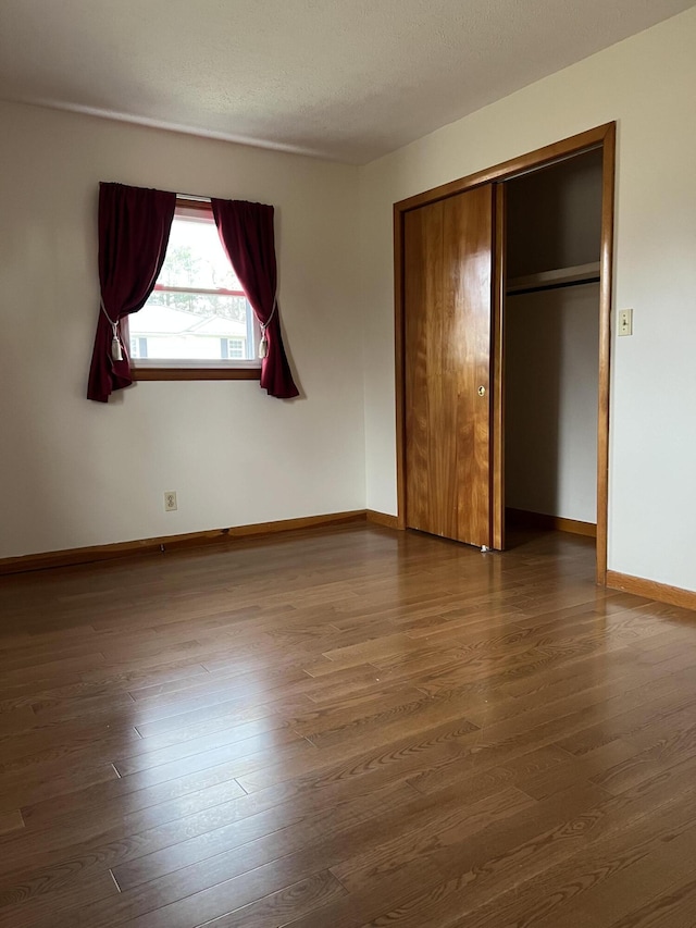 unfurnished bedroom featuring a textured ceiling, a closet, dark wood finished floors, and baseboards