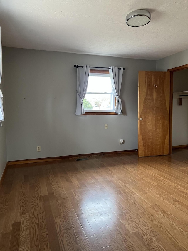 unfurnished room with light wood-type flooring, baseboards, and a textured ceiling