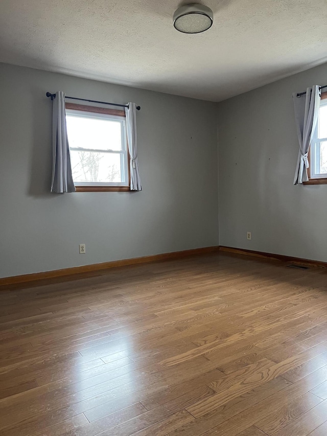 empty room featuring a wealth of natural light, a textured ceiling, baseboards, and wood finished floors