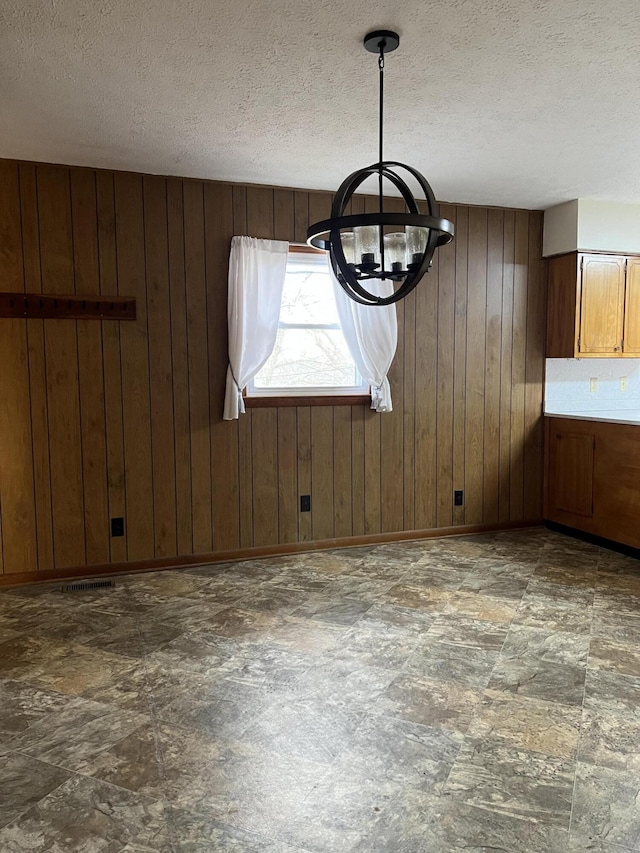 interior space with stone finish floor, a notable chandelier, wooden walls, and a textured ceiling