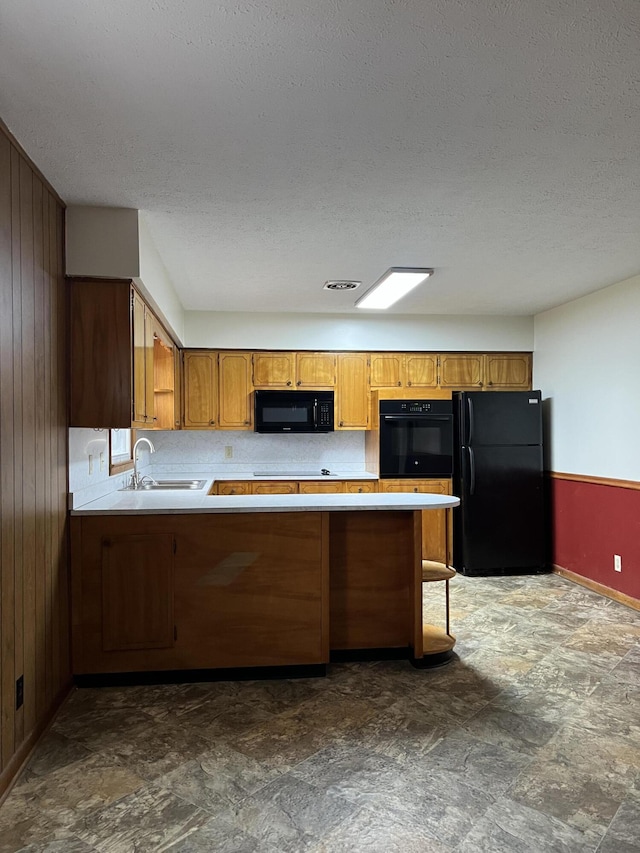 kitchen with a peninsula, light countertops, wood walls, black appliances, and a sink