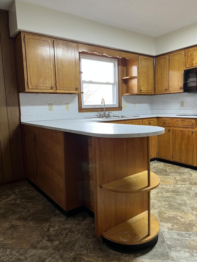 kitchen featuring brown cabinets, open shelves, light countertops, black microwave, and a peninsula