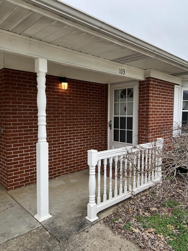 view of exterior entry featuring covered porch and brick siding