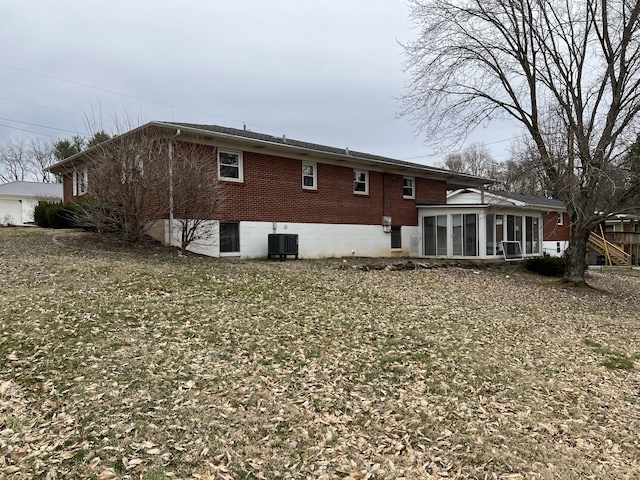 rear view of house with central AC unit, a garage, brick siding, a sunroom, and a lawn