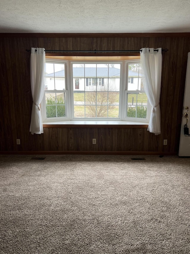 carpeted spare room with visible vents, a healthy amount of sunlight, wooden walls, and a textured ceiling