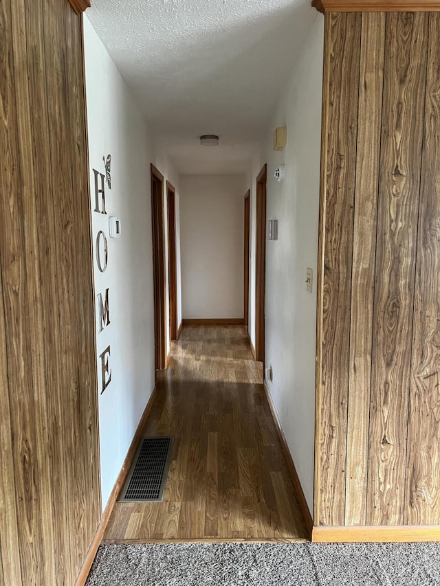 corridor featuring baseboards, visible vents, dark wood finished floors, and a textured ceiling