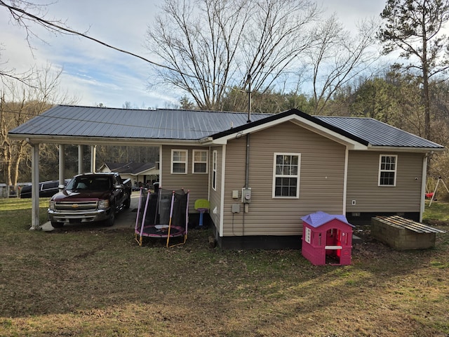 back of house featuring metal roof, a carport, a trampoline, and a lawn