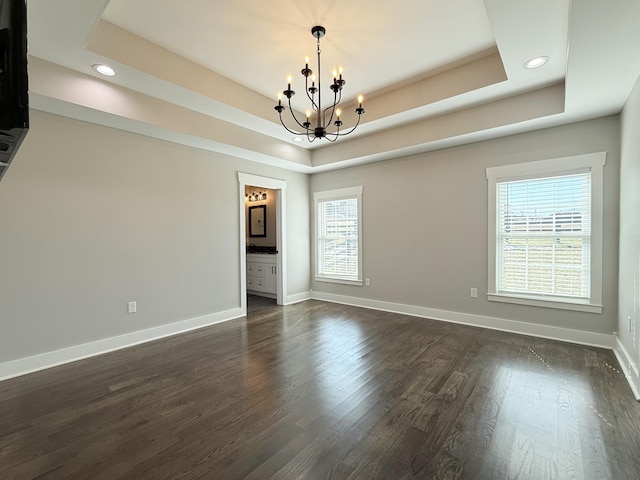 unfurnished room with a chandelier, a tray ceiling, dark wood-style flooring, and baseboards