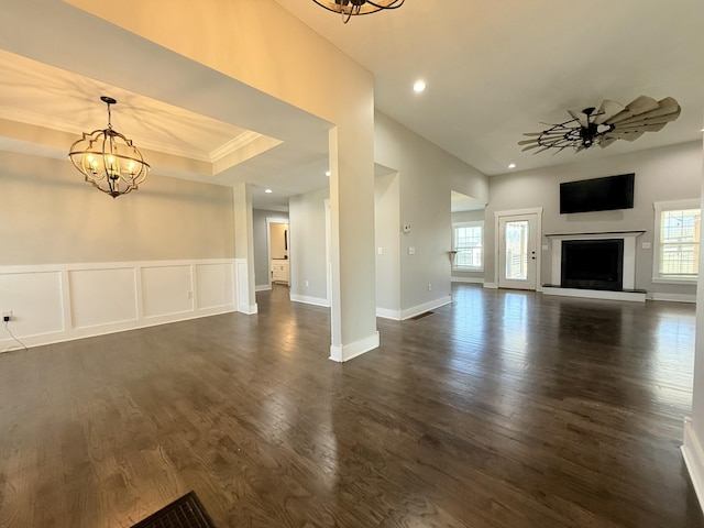 unfurnished living room with a fireplace with raised hearth, dark wood-style floors, ceiling fan with notable chandelier, a decorative wall, and recessed lighting