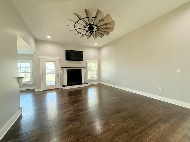 unfurnished living room featuring recessed lighting, a fireplace with raised hearth, dark wood finished floors, and baseboards