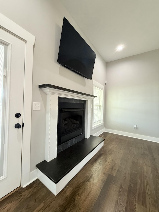 unfurnished living room featuring a fireplace with raised hearth, baseboards, and dark wood finished floors