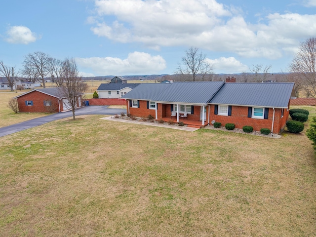 ranch-style home featuring aphalt driveway, brick siding, covered porch, a front yard, and metal roof