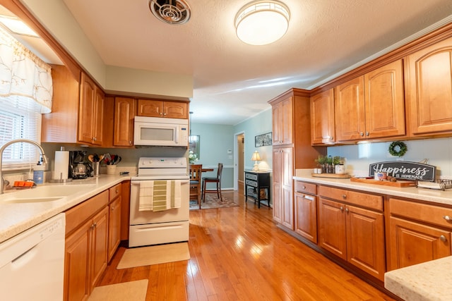 kitchen featuring light wood finished floors, light countertops, white appliances, and a sink